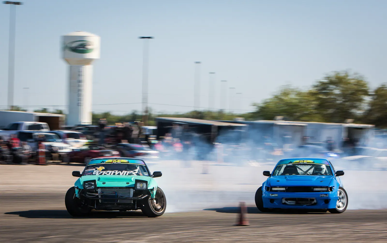 Two drift cars sliding side by side in a tandem battle with tyre smoke