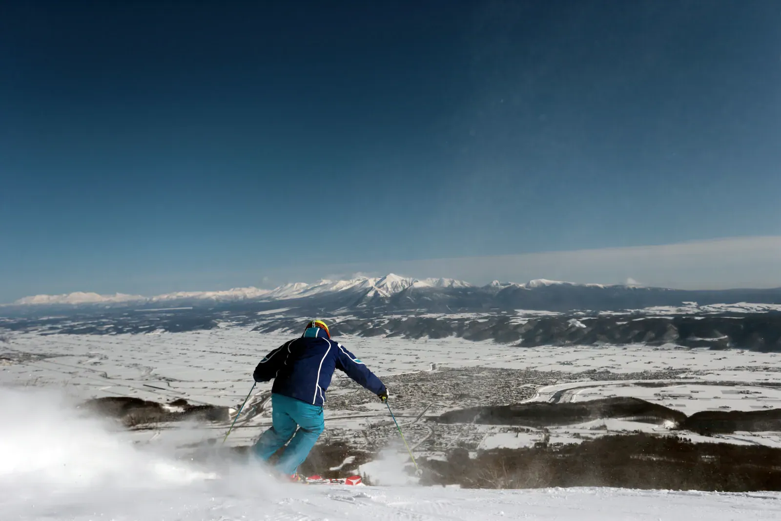Skier carving down a slope above the Furano valley and distant mountains