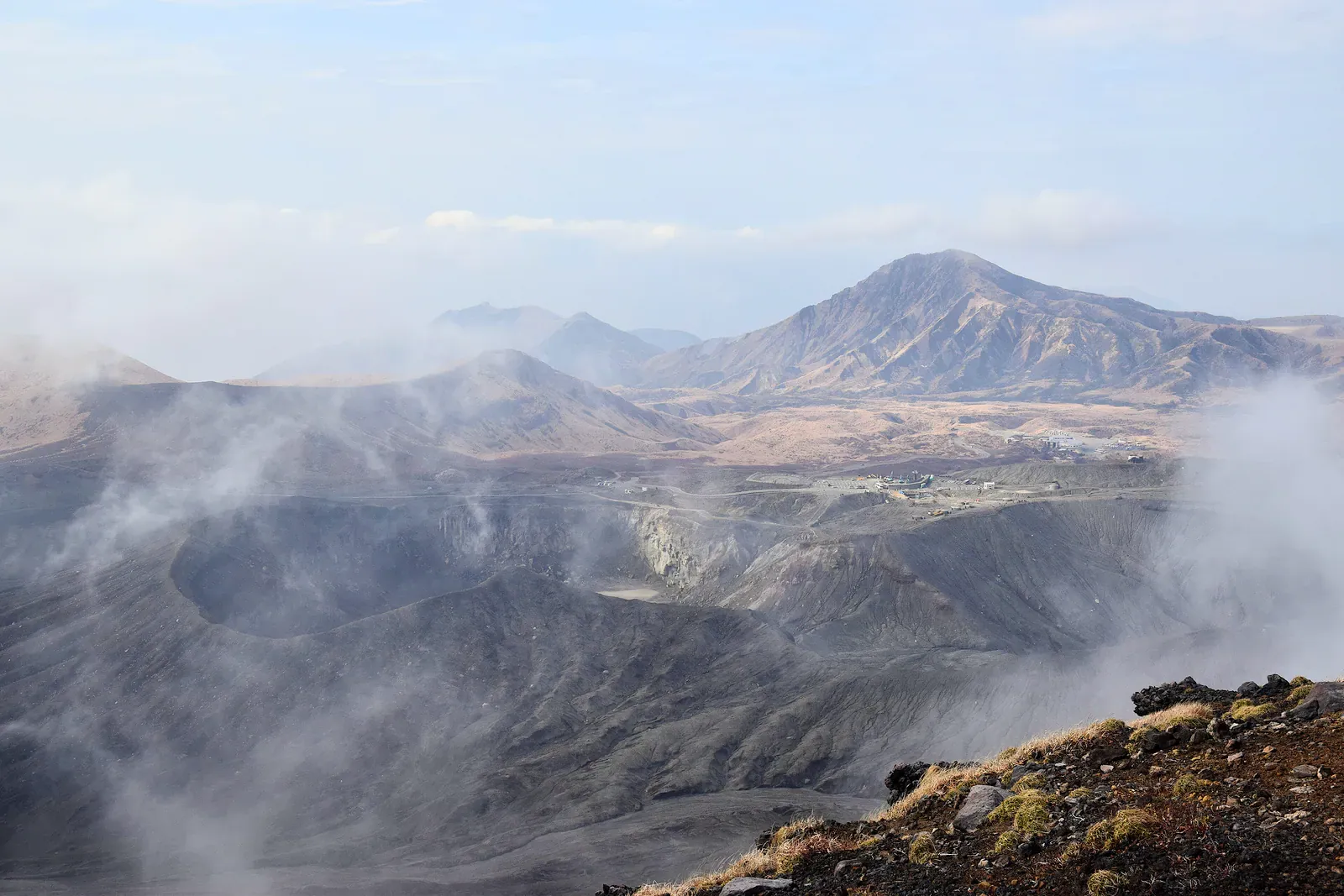 Steaming volcanic crater with grey ash slopes and peaks beyond
