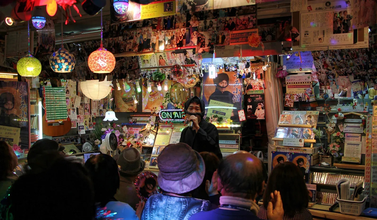 Crowd gathered at a cluttered collectibles stall hung with toys and posters