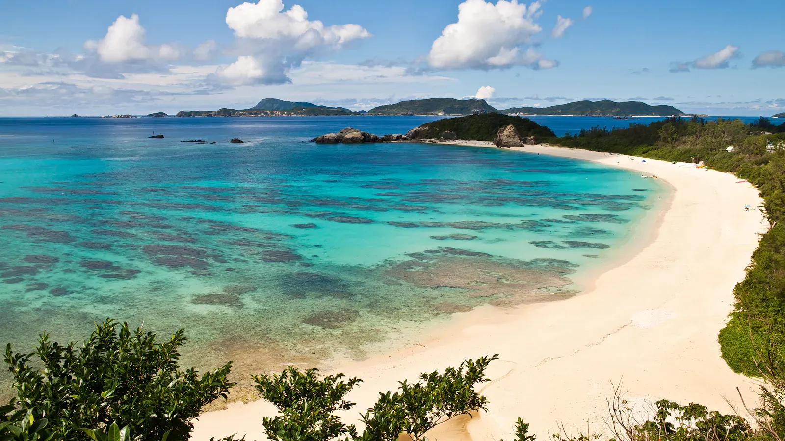 Curving white-sand Okinawa beach and turquoise lagoon seen from a headland