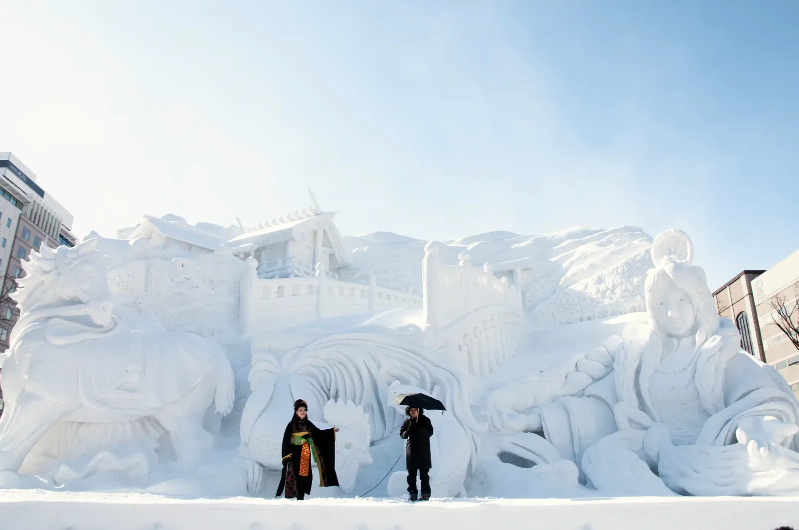 Huge carved snow sculpture with two visitors at the Sapporo Snow Festival in daylight